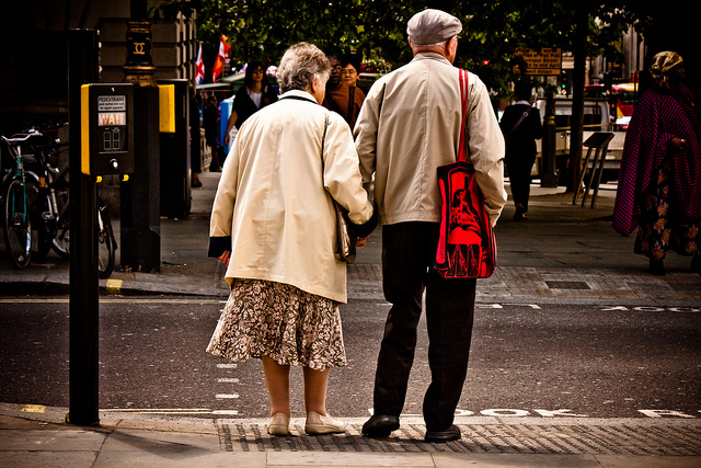 An elderly couple wait to cross the road